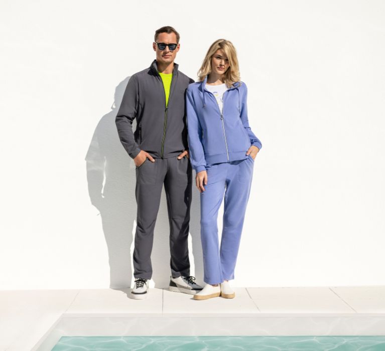 Mann und Frau stehen vor einem Pool und tragen Artikel der Marke JOY sportswear.